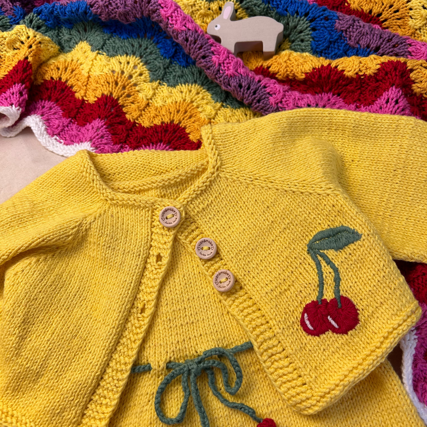 Yellow knitted cardigan with cherry design on a colorful knitted blanket