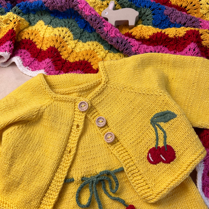 Yellow knitted cardigan with cherry design on a colorful knitted blanket
