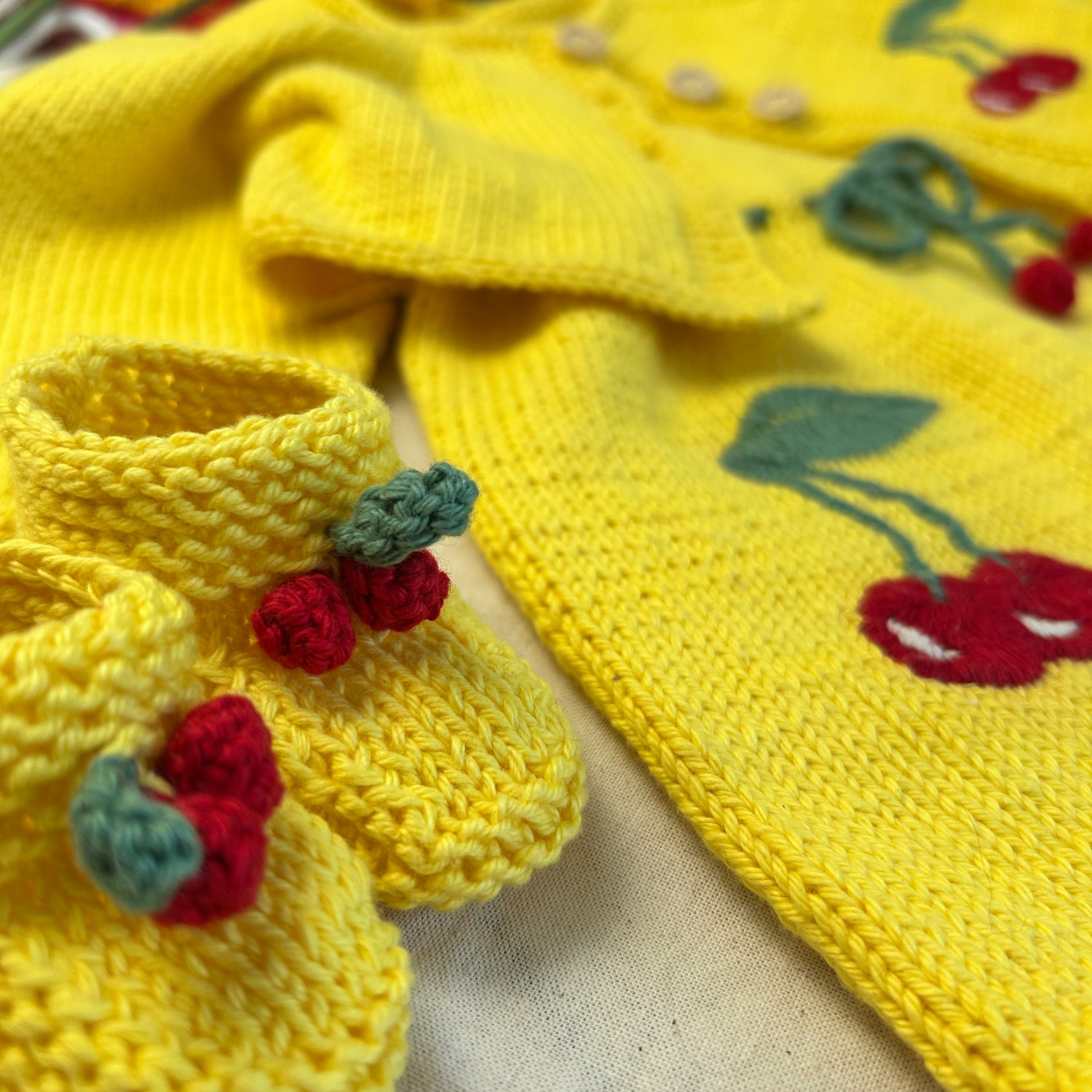 Yellow knitted baby outfit with cherry details on a beige background