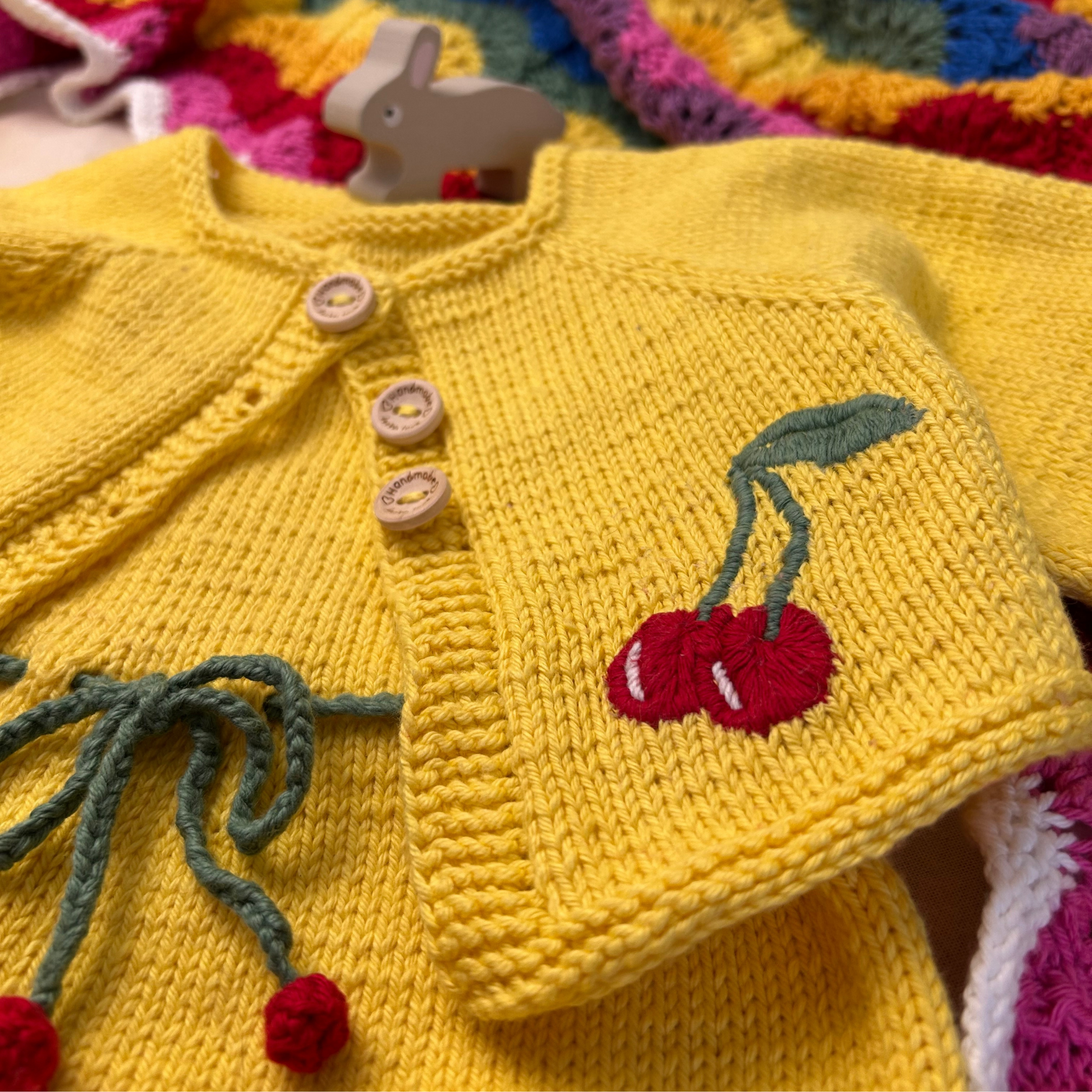 Yellow knitted cardigan with cherry design on a colorful fabric background