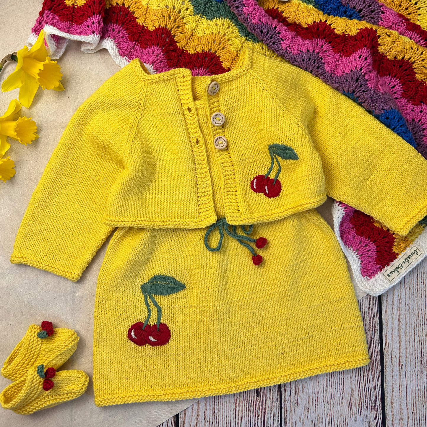 Yellow knitted baby outfit with cherry design on a wooden surface
