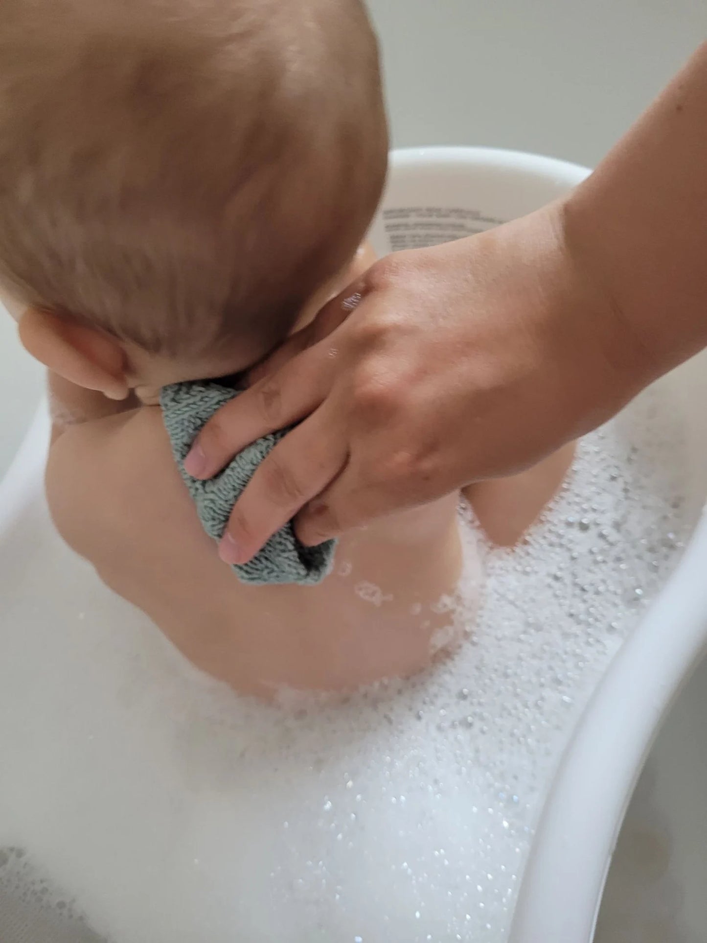 Child being bathed by an adult with a sponge in a bathtub filled with bubbles