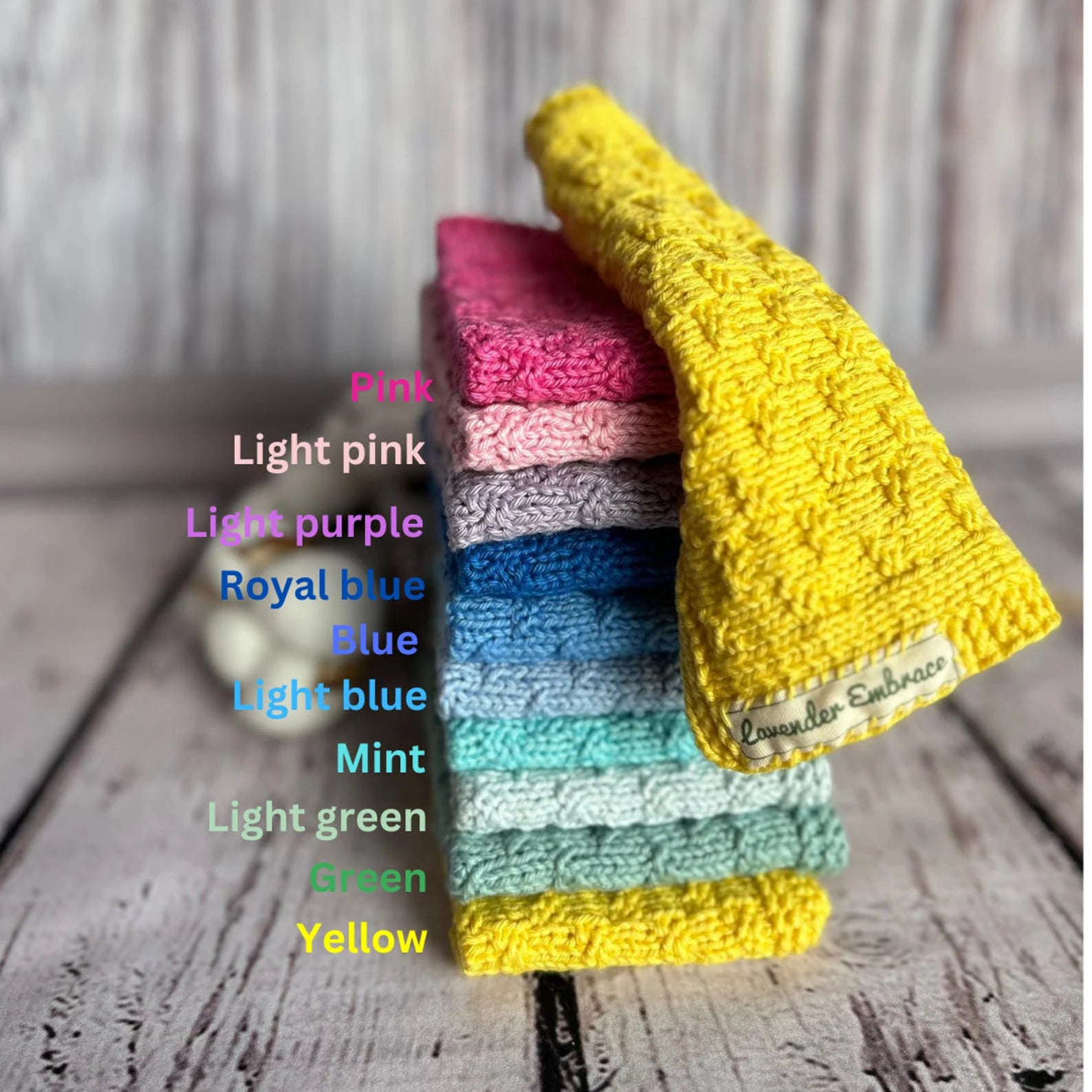Stack of colorful crocheted washcloths on a wooden surface with color labels.