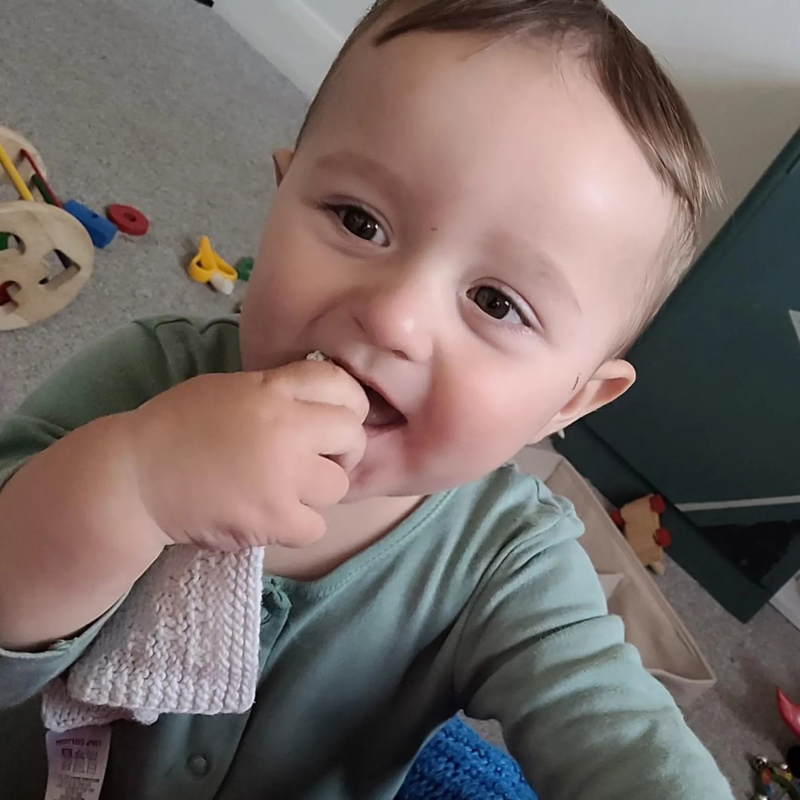 Baby chewing on a cloth with toys in the background