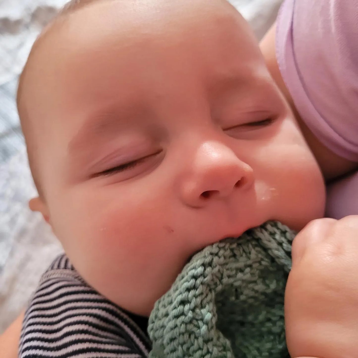 Close-up of a baby holding a green knitted item with a blurred background