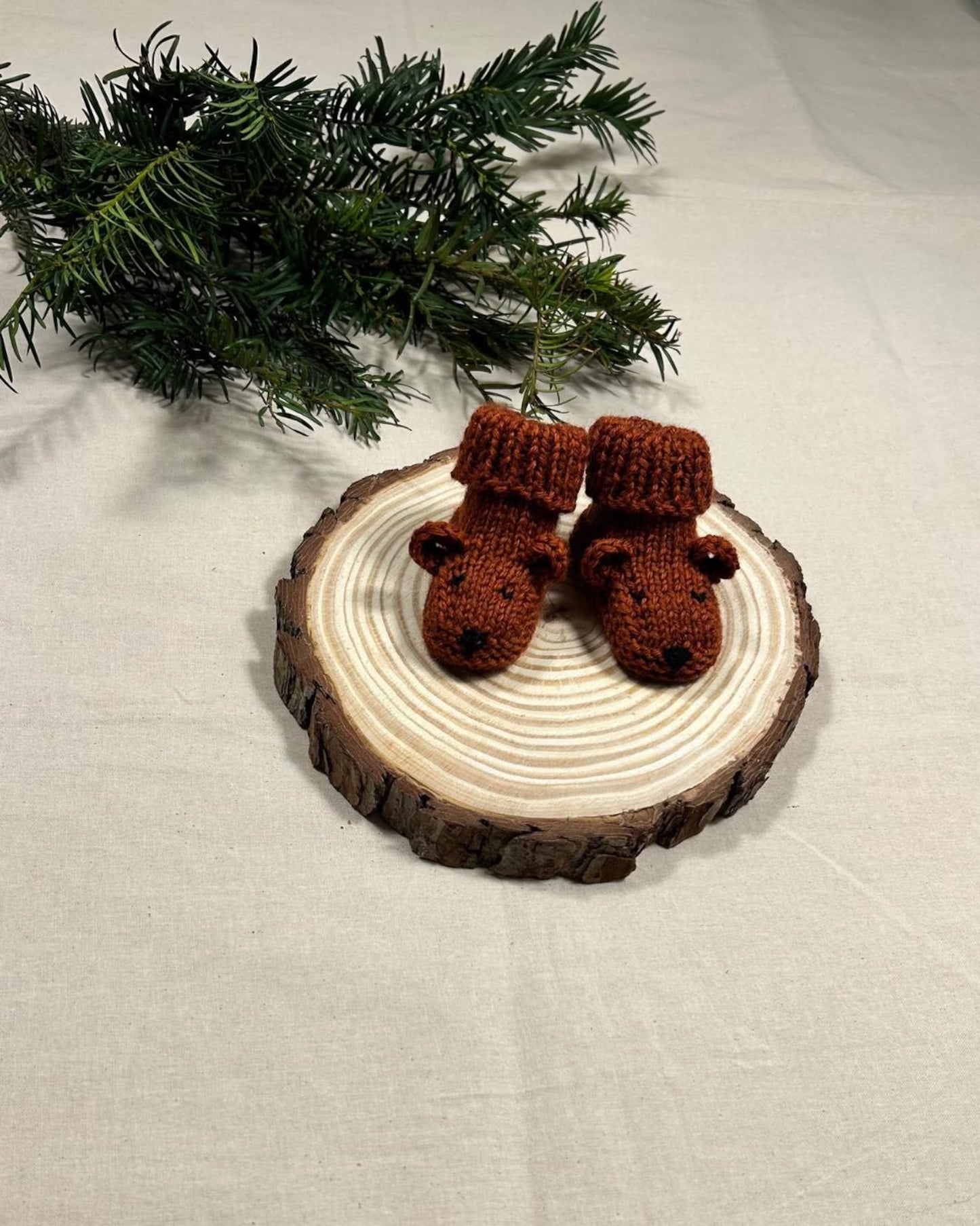 Pair of brown crocheted baby booties on a wooden disc with greenery in the background.