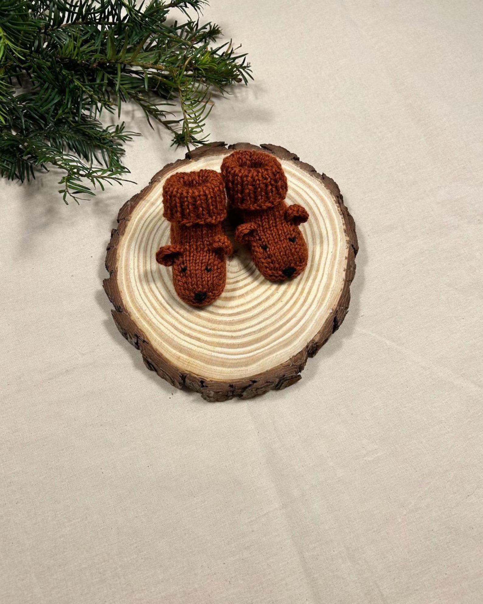Knitted brown bear ornaments on a wooden disc with a Christmas tree branch in the background.