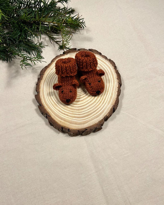 Knitted brown bear ornaments on a wooden disc with a Christmas tree branch in the background.