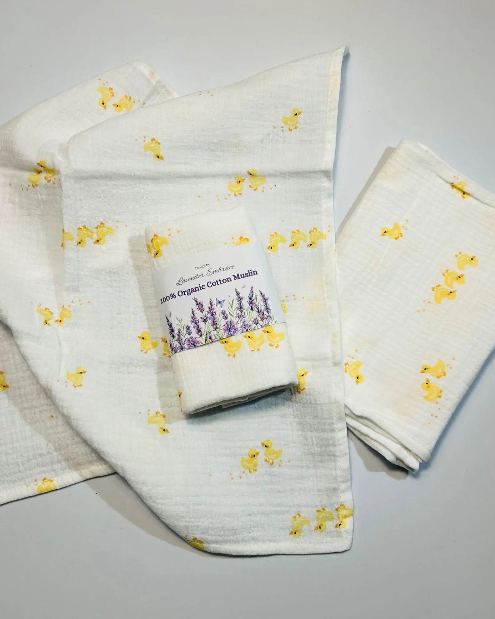 Muslin cloth with yellow floral pattern and a roll of organic cotton muslin on a gray background