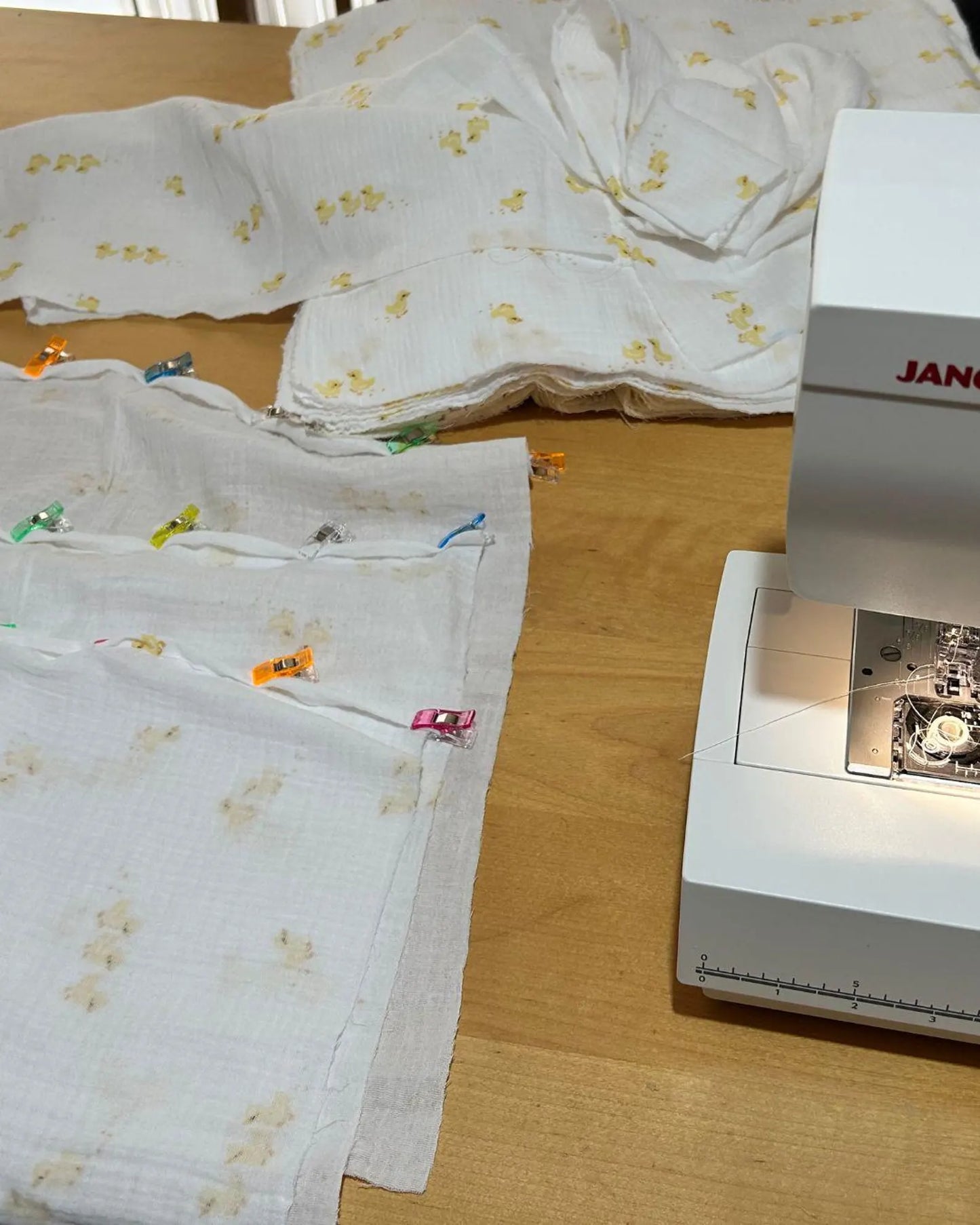 Fabric with floral patterns on a wooden table next to a sewing machine.