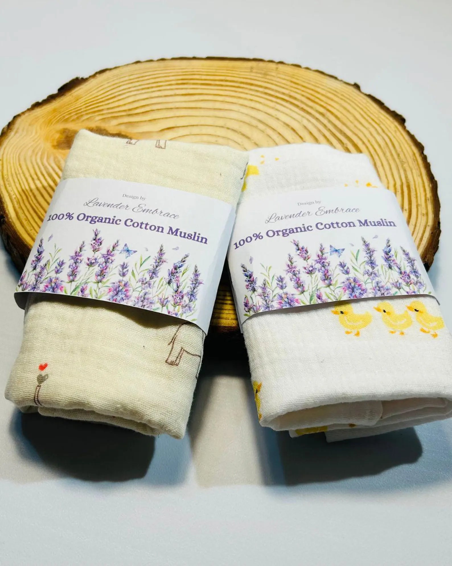 Two rolls of organic cotton muslin on a wooden block with lavender and chick design labels.